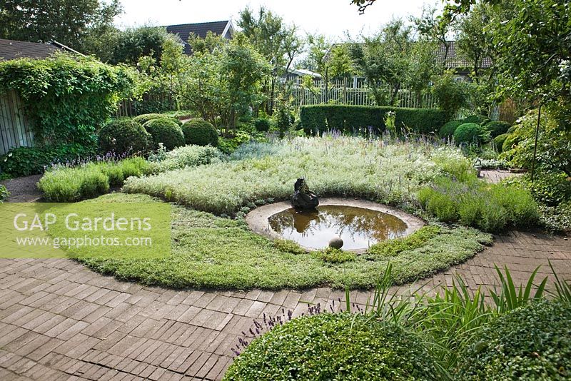 Circular pond surrounded by planting of Lavender, Anaphalis, Antennaria dioica, Apple and Plum trees, Buxus and Taxus topiary and hedges, Artemisia 'Silver queen', Brunnera, Lavender, Veronica spicata with brick and terracotta tile surfaces - Ulla Molin
 