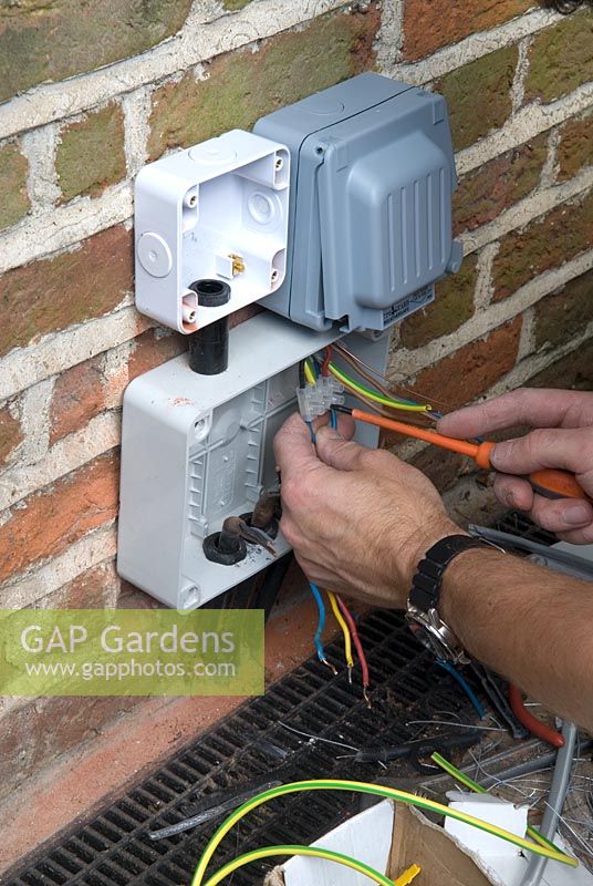 Making connections in mains jointing box on outside wall of cottage for garden lighting