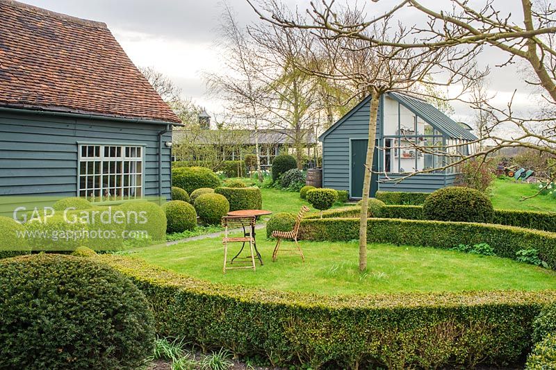 View to garden store and lean to greenhouse. Wrought iron garden table and seats. Yew and box topiary and dwarf hedges - The Mill House, Little Sampford, Essex