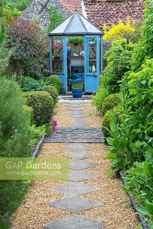 Cottage garden with slab and shingle path leading to hexagonal greenhouse