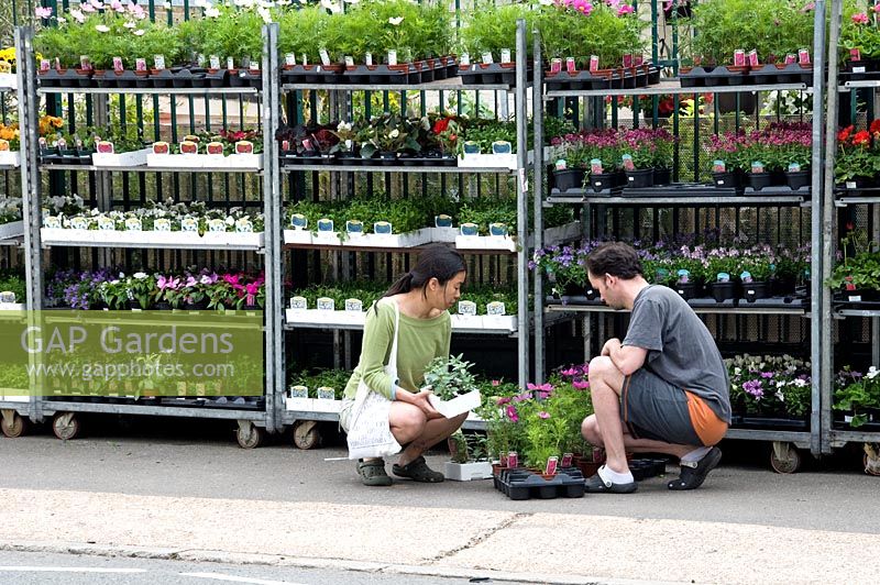 Young couple choosing plants outside urban garden centre with plants displayed in street, N1 Garden Centre, London Borough of Hackney, UK