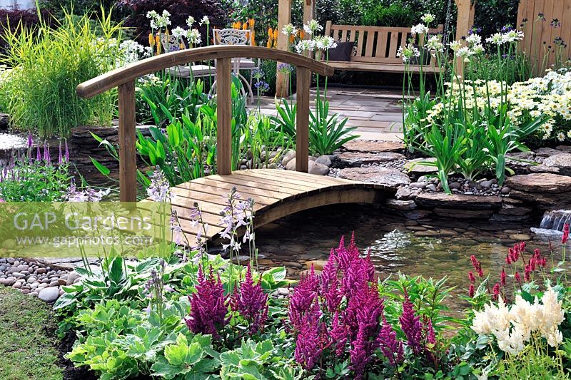 Wooden Bridge over pond. Agapanthus and astilbe along stream. The Water garden. RHS Tatton Park Flower show 2013