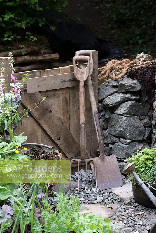 Old tools in the Motor Neurone Disease - A Hebridean Weavers Garden - wooden gate, garden fork, spade, bucket of sea weed and stone wall