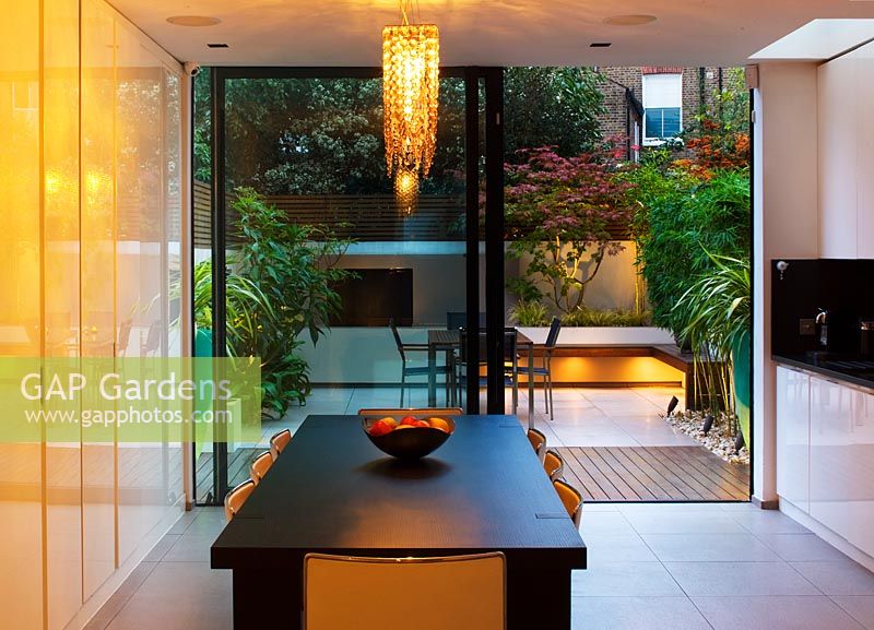 View out of kitchen to modern, minimalist garden lit up at night 