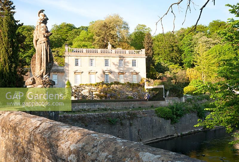 Iford Manor, a Georgian house, sitting in a steep sided valley beside the River Frome, seen from the bridge, dating from 1400, topped by an 18th century statue of Britannia installed by Peto