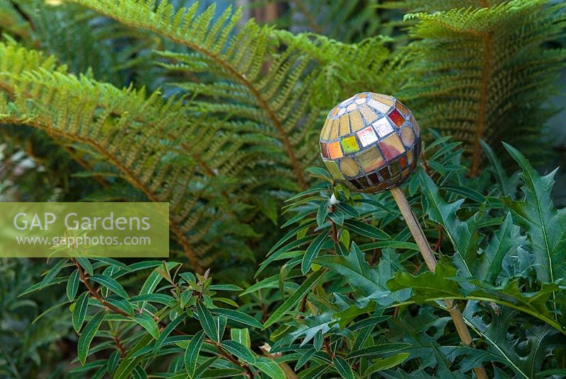 Mosaic ball on stick, designed by Anne Cardwell, in the border with ferns and Acanthus leaves in town garden