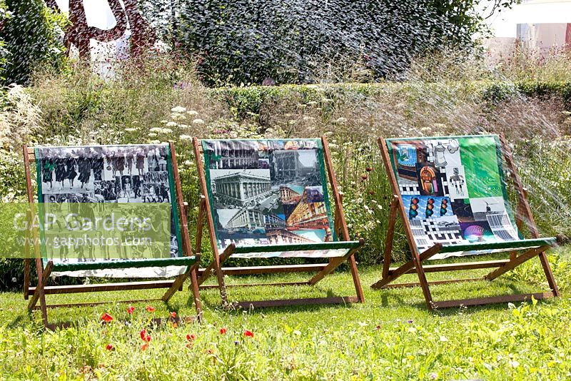 Sprinkling water over three Garden chairs with colour prints.