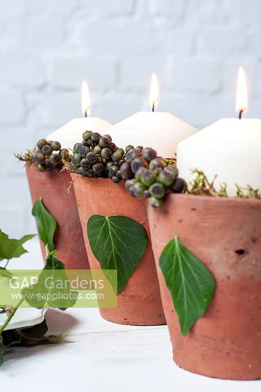 Candles in decorated terracotta pots with hedera helix leaves and berries - ivy and moss