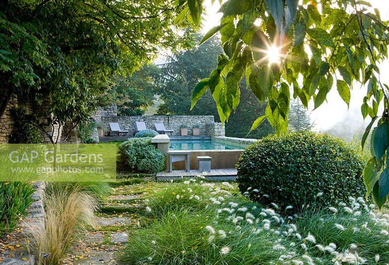 Swimming pool at dawn on the lower terrace with stone path and countryside beyond 
