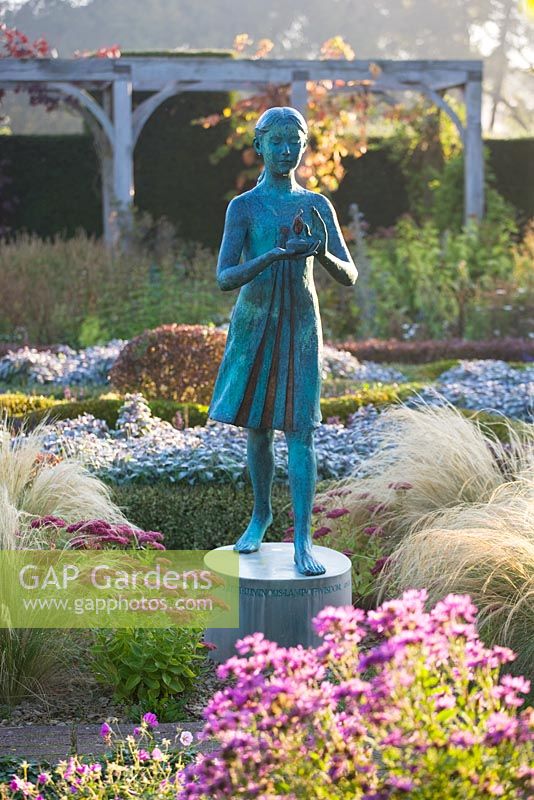 The hedged in formal garden at dawn with box and berberis hedging and topiary - girl statue called the 'lamp of wisdom'. Waterperry Gardens, Oxfordshire
