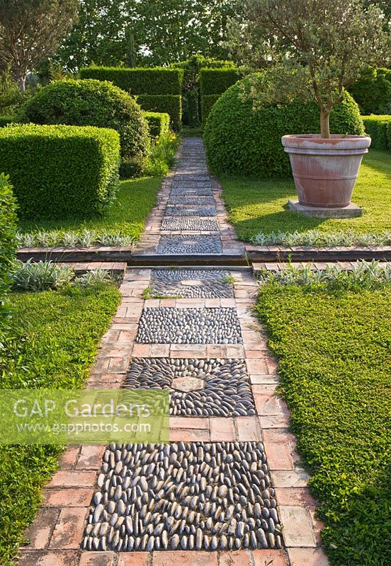 Pebble and brick pathway through clipped hedges and lawn 