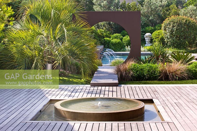 Modern contemporary garden - decking, water feature, metal 'Oculus' circle and swimming pool. Les Confines, Provence, France