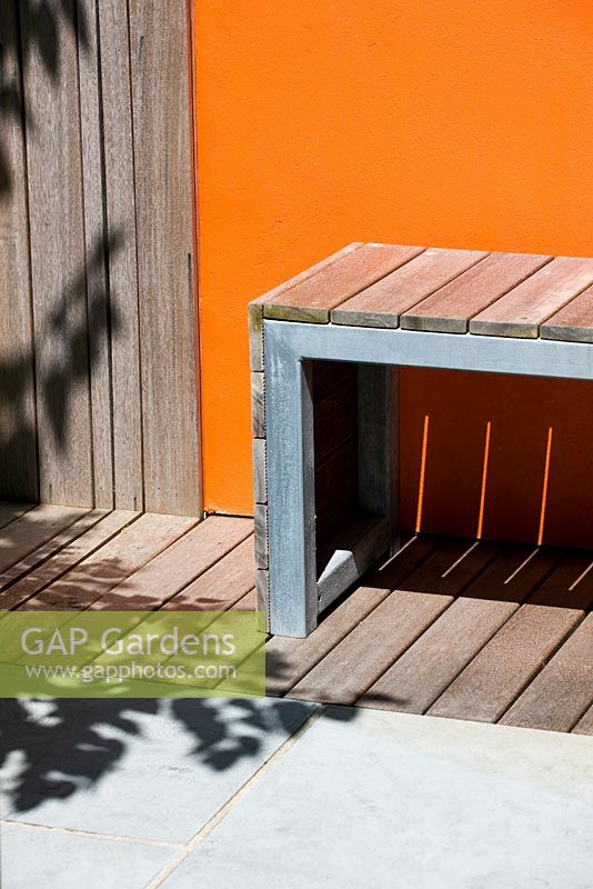 Modern contemporary garden in Brighton with decking, orange panels on walls, wooden bench and shadows