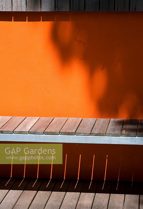 Modern contemporary garden in Brighton with decking, orange panels on walls, wooden bench and shadows

