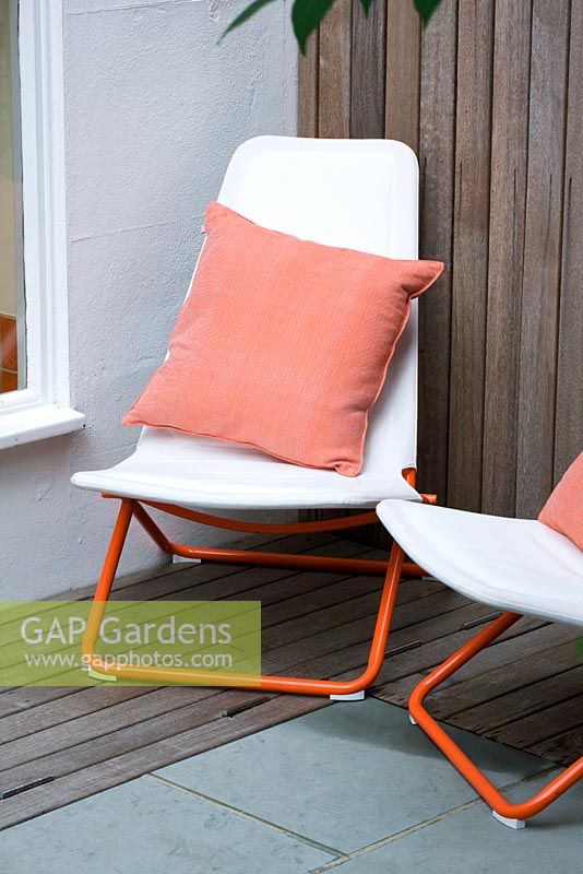 Modern contemporary garden in Brighton with white deckchairs on decking with orange cushions 