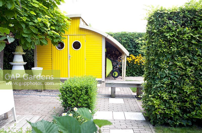 Bright yellow shed with roundshaped windows. Rudbeckia fulgida Goldsturm in the border.