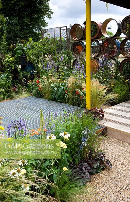 Metal. A Space to Connect and Grow. View cross geometric layout of garden towards boundary fence with creative use of recycled materials including drying machine drums. Mesh flooring. Colourful mid summer planting. Designer: Jeni Cairns and Sophie Antonelli Sponsor: Metal Gold award best summer garden