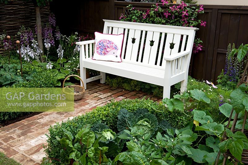 Hedgehog Street white wooden bench set on brick path flooring between box-edged vegetable beds with cabbage and potatoes.  Designer: Tracy Foster Sponsor: People's Trust for Endangered Species. Gold award  