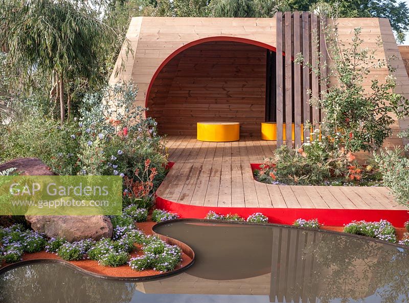 Essence of Australia - view of Australian garden pond pool surrounded by Brachyscome blue with decking and summer shelter with wooden seats - Designer - Jim Fogarty for Royal Botanic Gardens Melbourne - Sponsor - Tourism Victoria - Tourism Northern Territory - Qantas - Trailfinders