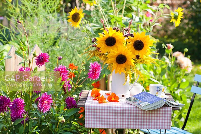 Bouquet of  sunflowers and perennials Persicaria, Verbena bonariensis and Solidago in enamel jug in summer garden.