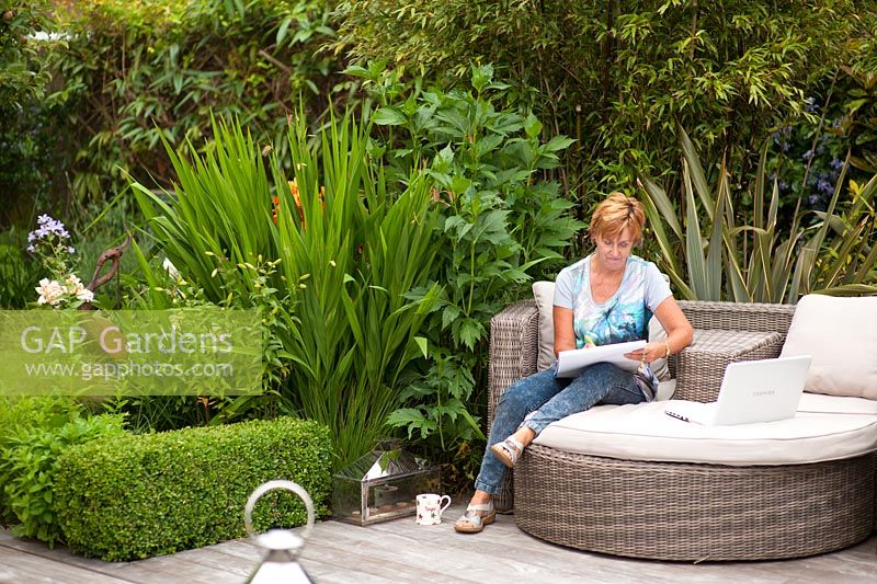 Garden designer Angie Barker sketching in her garden with planting of Phormiums, Crocosmia 'Lucifer' and Lilies restrained by a low Buxus sempervirens hedge
