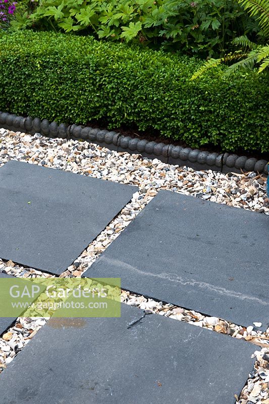 Contrasting textures of 20ml gravel Moonstone with slate natural stone paving in squares before blue rope edging and low Box hedging