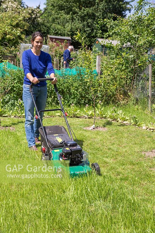 Woman mowing grass on an allotment patch