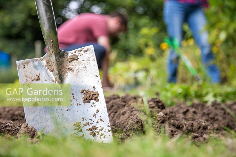 Spade embedded in soil, man and woman working in background