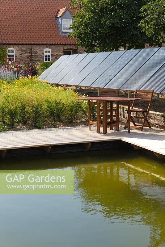 A solar panel installation in a garden setting next to waters edge - August, Summer 2014.