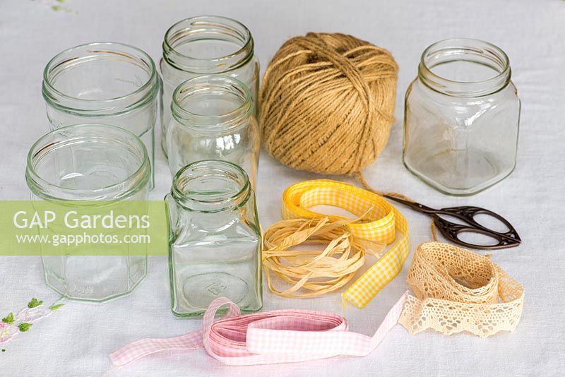 Decorating glass jars for garden posies step by step. Assorted empty glass jars with gardener's jute twine string, gingham ribbon, raffia and cotton lace for decoration.
