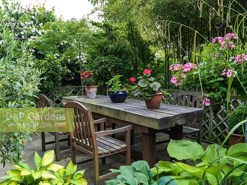 A private patio seating area with chunky wooden table and chairs in a very small space. Large-scale furnishings, as opposed to lots of little bits, increase the sense of roominess in a confined space. Tall bamboo screens the seating from the main garden.