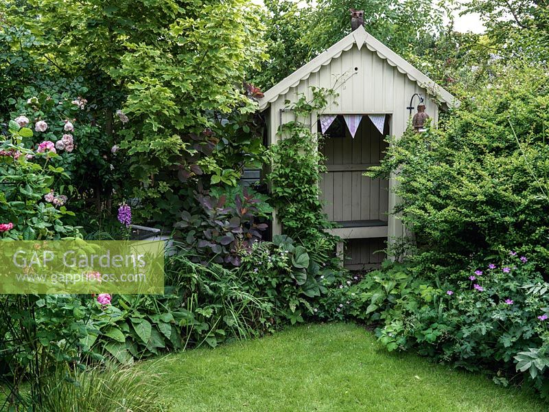 A traditional summer garden with borders filled with roses and perennials with a wooden arbour.