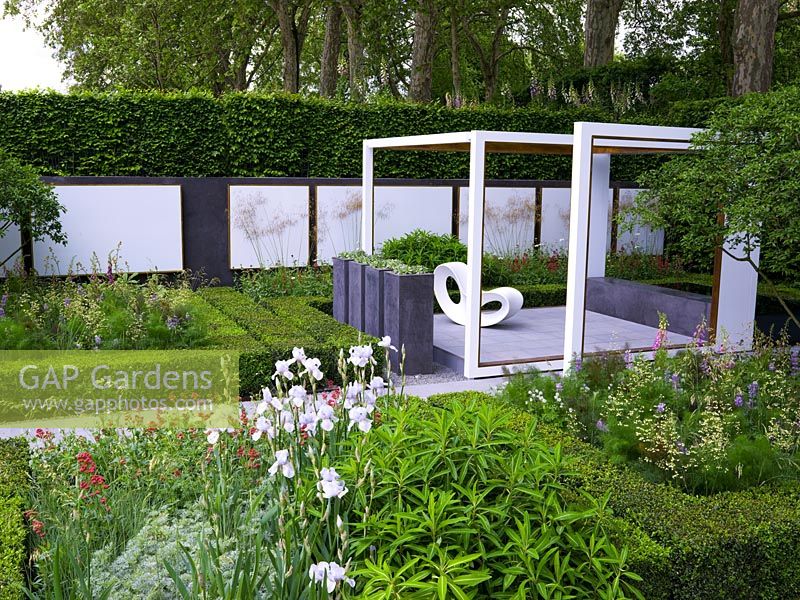 Pergola-like wooden frames focus attention on views within the space. Geometric layout of box and hornbeam mixes with perennials and shrubs. Raised patio with chair.