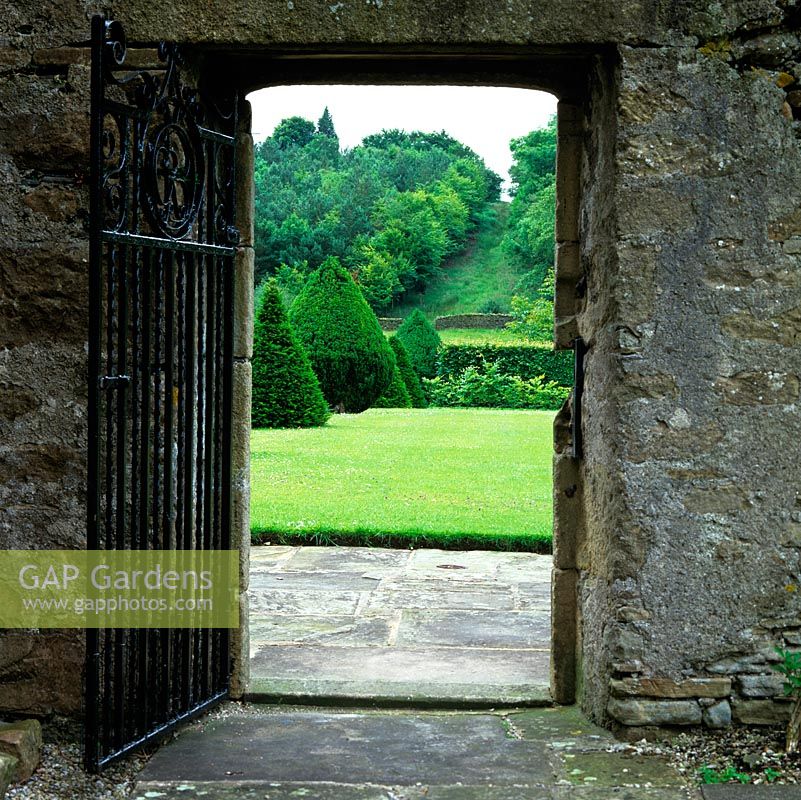 Ancient gateway in stone wall frames view of yew topiary and distant hillside.