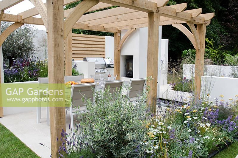 Seating area under pergola with BBQ and outdoor woodburner, Olearia x haastii in a border with Echinacea 'White Swan', Achillea 'Walther Funcke', Carex testacea, Nepeta 'Walkers Low' and Orlaya grandiflora, Al Fresco, RHS Hampton Court Palace Flower Show 2014 