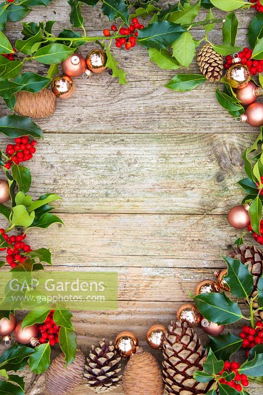 Wooden surface with a border of Copper baubles, Pine cones and Ilex aquifolium foliage.