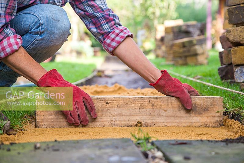 Use a plank of wood to level the sand. Making a brick path