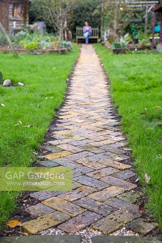 Woman sat on a garden bench at the end of the new brick path. 