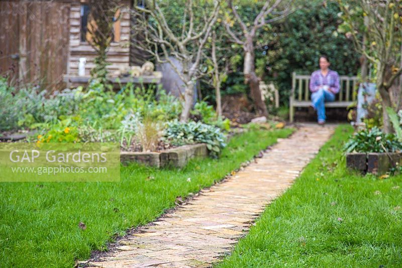 Woman sat on a garden bench at the end of the new brick path. 