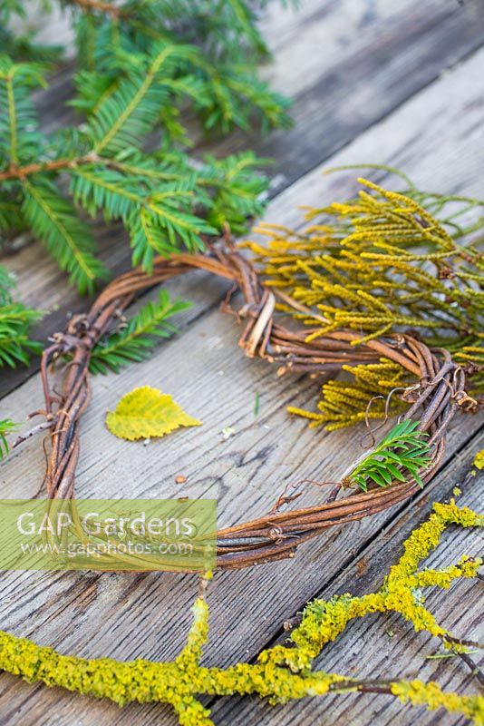 A grapevine heart on a wooden surface, accompanied with Yew foliage, Prunus with Lichen and Conifer foliage