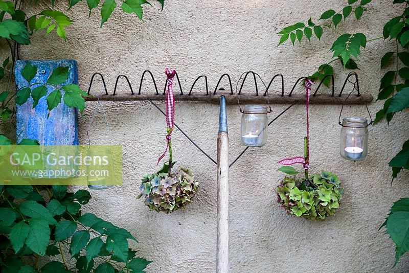 Garden rake decorated with hydrangea flowerheads and tealight candles in jars against a wall