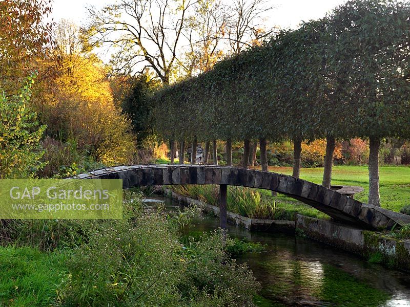 A wooden footbridge crosses a mill stream linking two sections of a country garden.