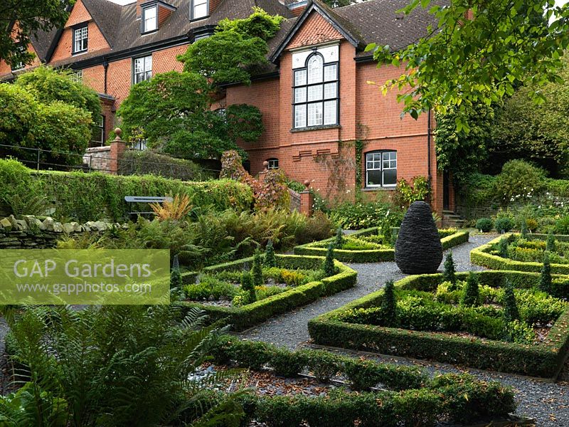 In a shady, sloping corner by the Arts and Crafts house, a recently established parterre of box and lonicera topiary and hedges, infilled with slate shards.