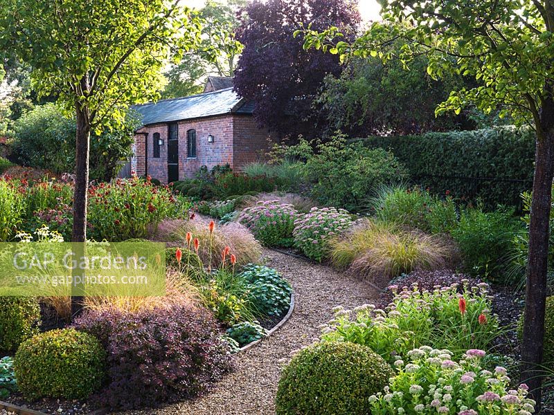 Beds of Pyrus calleryana Chanticleer, Sedum Autumn Joy, echinacea, hardy geranium, Kniphofia Nancy's Red, cercis, box balls, Stipa arundinacea, berberis, Helenium Moerheim Beauty, Miscanthus sinensis.