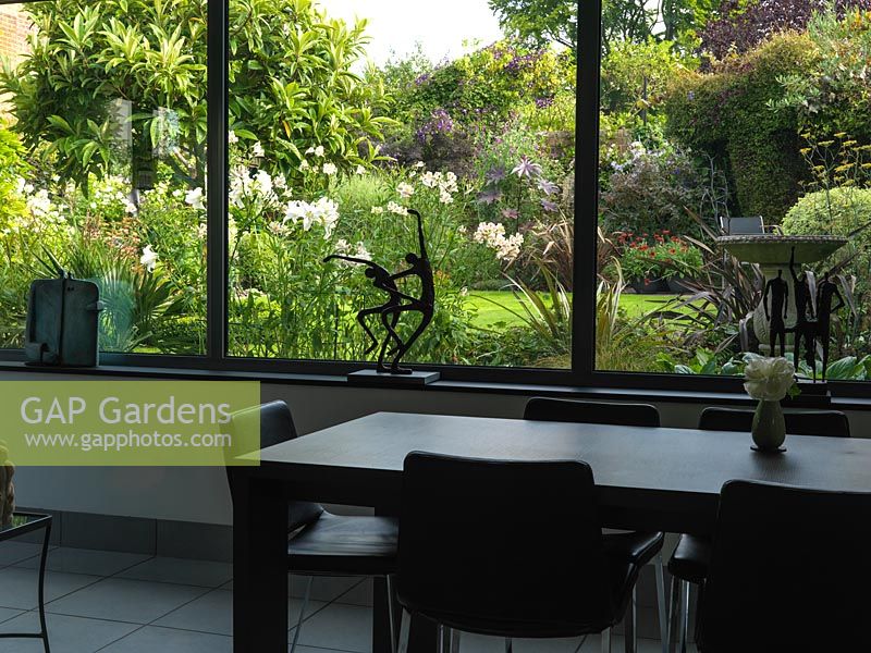 From kitchen, dining room, picture window frames view of small garden with loquat tree and near bed of white lilies and alstroemeria, phormium, pittosporum and fennel. The effect of the view from window is both to draw the garden in, and to make the room seem more spacious.