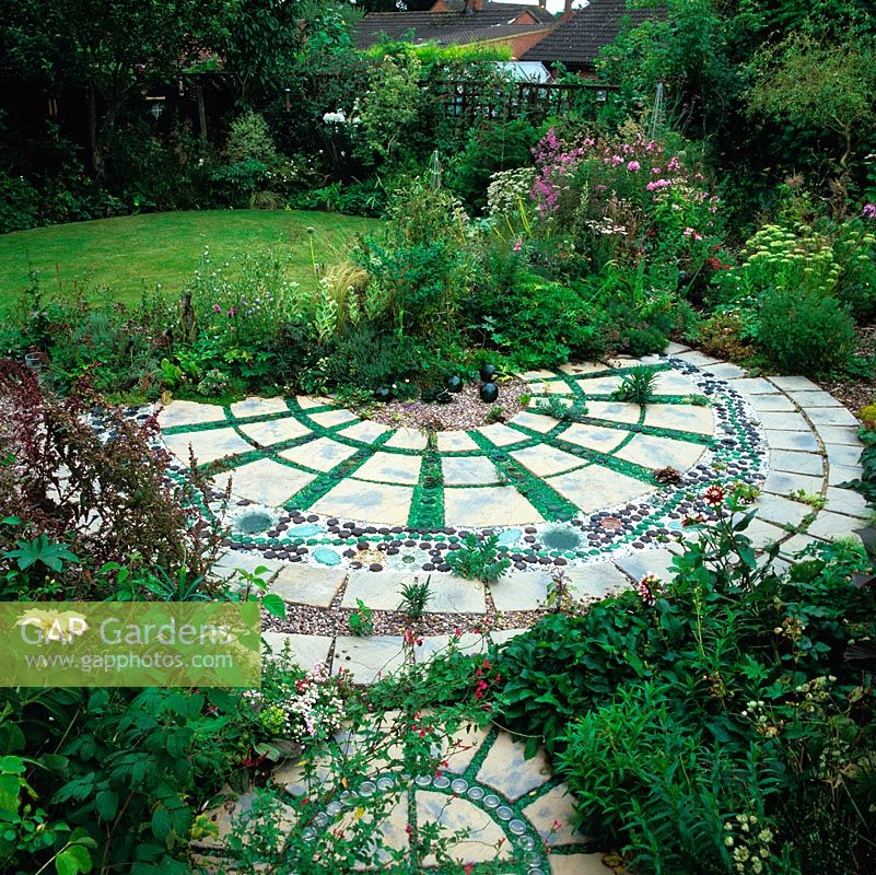 Curving patio made from paving slabs interspersed with 800 glass bottles and dishes. At its heart, gravel area with glass buoys.