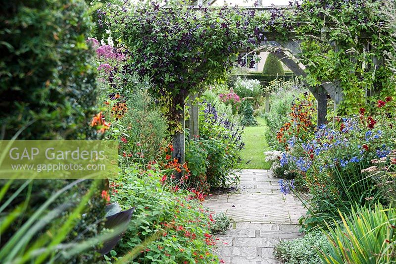 View into Sundial Garden framed by clematis covered pergola, heleniums, monardas, agapanthus and salvias, with asters full of buds beyond. Wollerton Old Hall, nr Market Drayton, Shropshire, UK