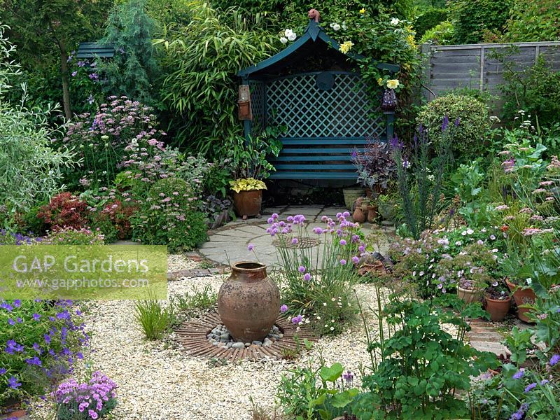 A circular themed gravel garden and patio with cottage garden style planting. Armeria Joystick and a terracotta urn provide a focal point in the centre of the gravel bed. 