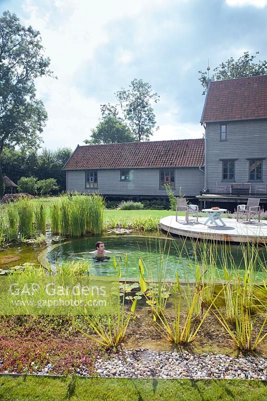 View of a house with outside decking and the swimming pond with a man swimming in it.