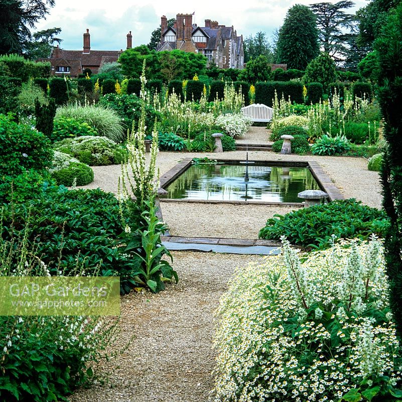 Formal pond in the White Garden with verbascum, Tanacetum niveum, hebe, hydrangea, hosta, rose and bamboo. Behind, Elizabethan manor house.